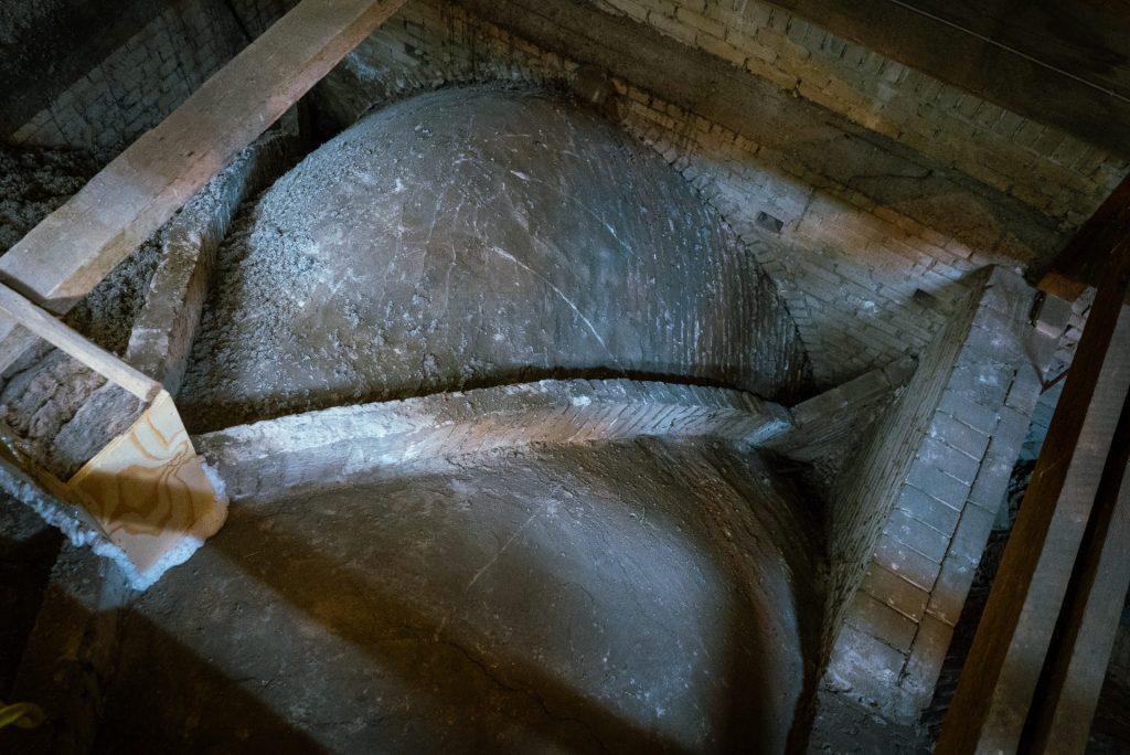 Een grote, oude waterketel of tank in een industriële omgeving, omgeven door bakstenen muren en houten balken, geschikt voor isolatie- en onderhoudsdoeleinden.